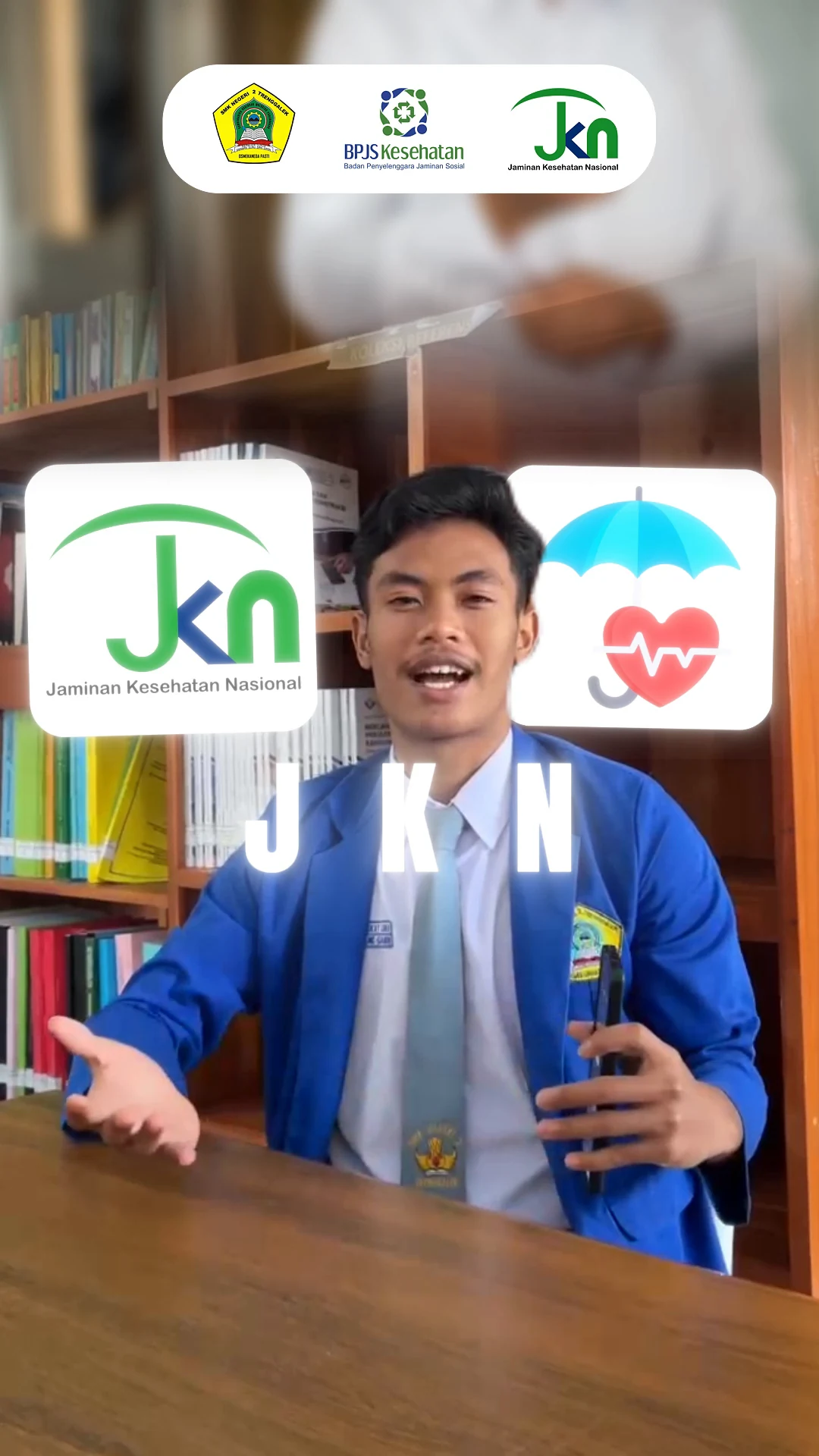 Cuplikan adegan edukasi di ruang perpustakaan dengan overlay ikon payung kesehatan dan logo JKN.